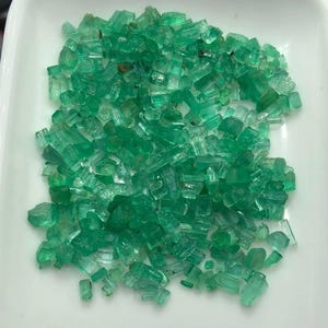 Puede incluir: Un montón grande de piedras preciosas de esmeralda verde en bruto. Las esmeraldas son de varios tamaños y formas, algunas son largas y delgadas, mientras que otras son más redondeadas.