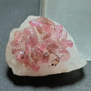 May include: A cluster of raw, translucent pink tourmaline crystals embedded in a jagged, opaque white quartz matrix. The pink mineral fragments are irregularly shaped with sharp edges and varying shades of rose, contrasting against the pale stone.