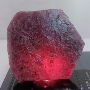 Peut inclure: Une grosse pierre précieuse de rubis rouge brute avec une couleur profonde et riche. Le rubis a une finition naturelle non polie et est éclairé par le bas, mettant en évidence sa structure interne.