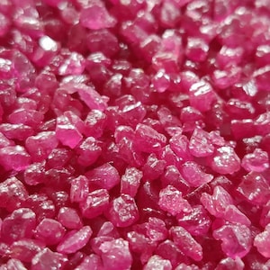 May include: A close-up view of a pile of small, rough, pink ruby gemstones.
