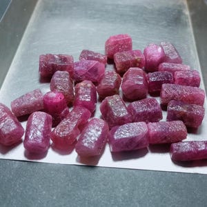 Puede incluir: Una colección de piedras preciosas de rubí rosa de varios tamaños y formas, expuestas en una bandeja de plata.