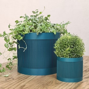 Op de afbeelding: Twee teal groene cilindrische potten met verticale lijnen, een groter dan de andere, beide gevuld met groene planten.