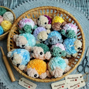 May include: A collection of small, plush, crocheted turtles in various pastel and vibrant colors, including blue, green, yellow, and pink, arranged inside a round woven basket. Each turtle features black plastic eyes and soft yarn texture.