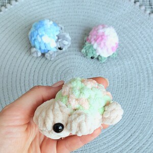 May include: Three small, handmade crochet turtles crafted from soft, plush yarn. One turtle features a cream-colored body with a pastel green and peach shell, while the others display blue and white or pink and green color combinations.