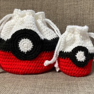 May include: Two crocheted Pokeball drawstring bags, one red, white, and black, and one smaller, in the same colors.