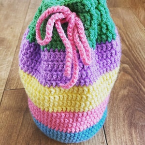 May include: A colorful crocheted drawstring bag with a pink, green, purple, yellow, and blue striped pattern.