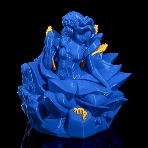 May include: A blue 3D printed figurine of the astrological sign Virgo. The figurine is a woman with long hair and a flowing dress, sitting on a bed of blue crystals. The sign Virgo is printed in gold on the base of the figurine.