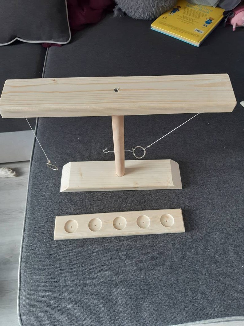 May include: Wooden ring toss game with a base, a vertical post, and a horizontal bar. The game has five holes for the rings to land in.