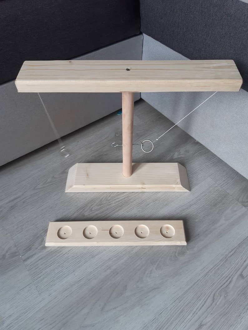 May include: Wooden ring toss game with a base, a vertical post, and a horizontal bar. The game includes five rings and a string attached to the bar.