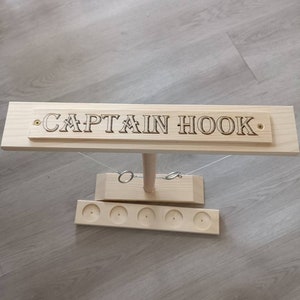 May include: Wooden Captain Hook ring toss game with a wooden base and five holes for the rings. The game has a sign that says "CAPTAIN HOOK" on it.