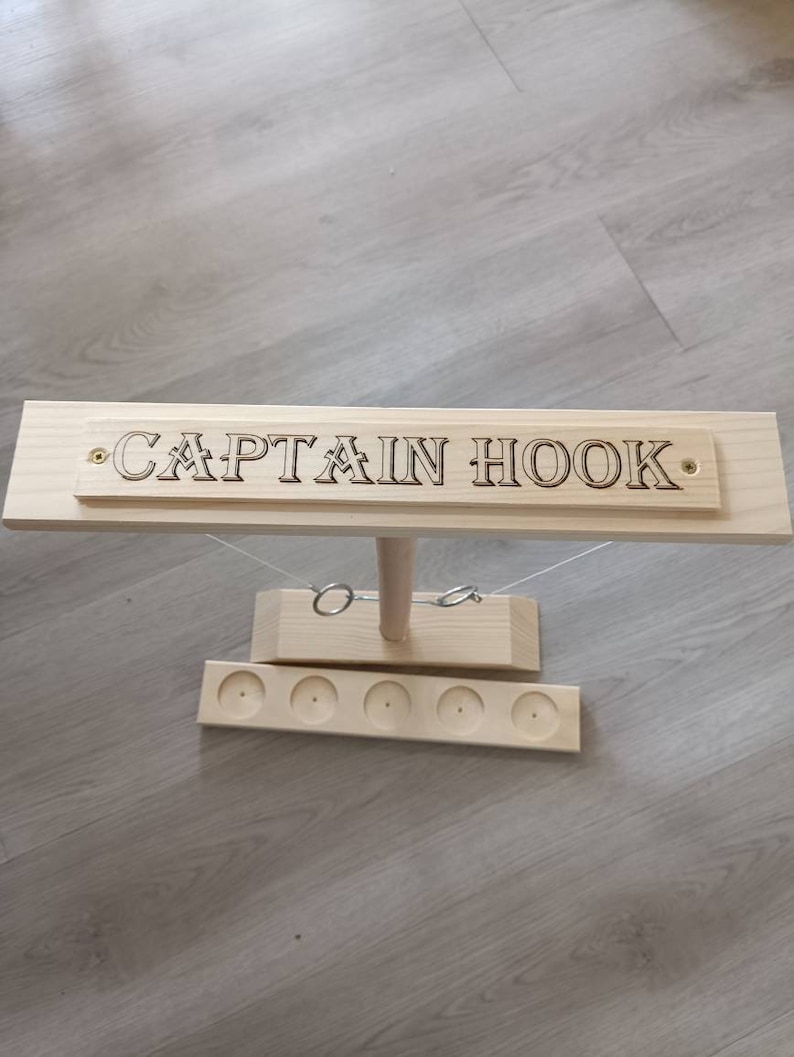 May include: Wooden Captain Hook ring toss game with a wooden base and five holes for the rings. The game has a sign that says "CAPTAIN HOOK" on it.