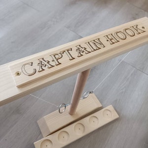 May include: Wooden Captain Hook game with a wooden base and six holes. The game includes two rings that hang from strings attached to a wooden pole.