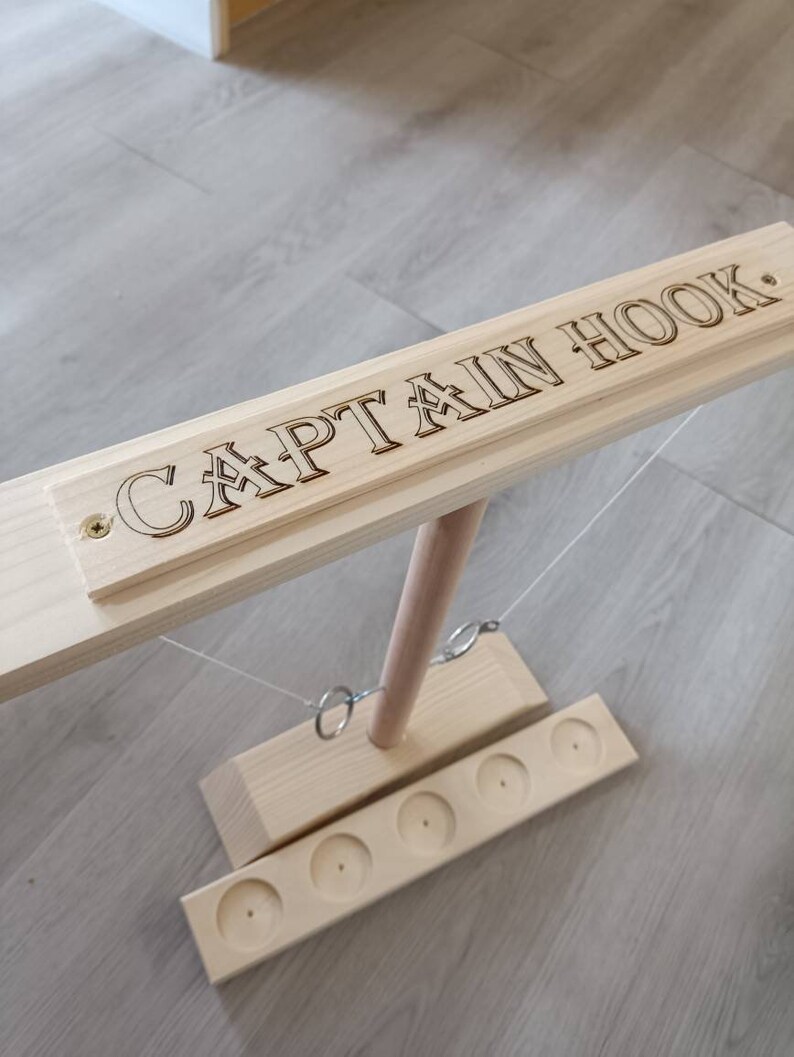 May include: Wooden Captain Hook game with a wooden base and six holes. The game includes two rings that hang from strings attached to a wooden pole.