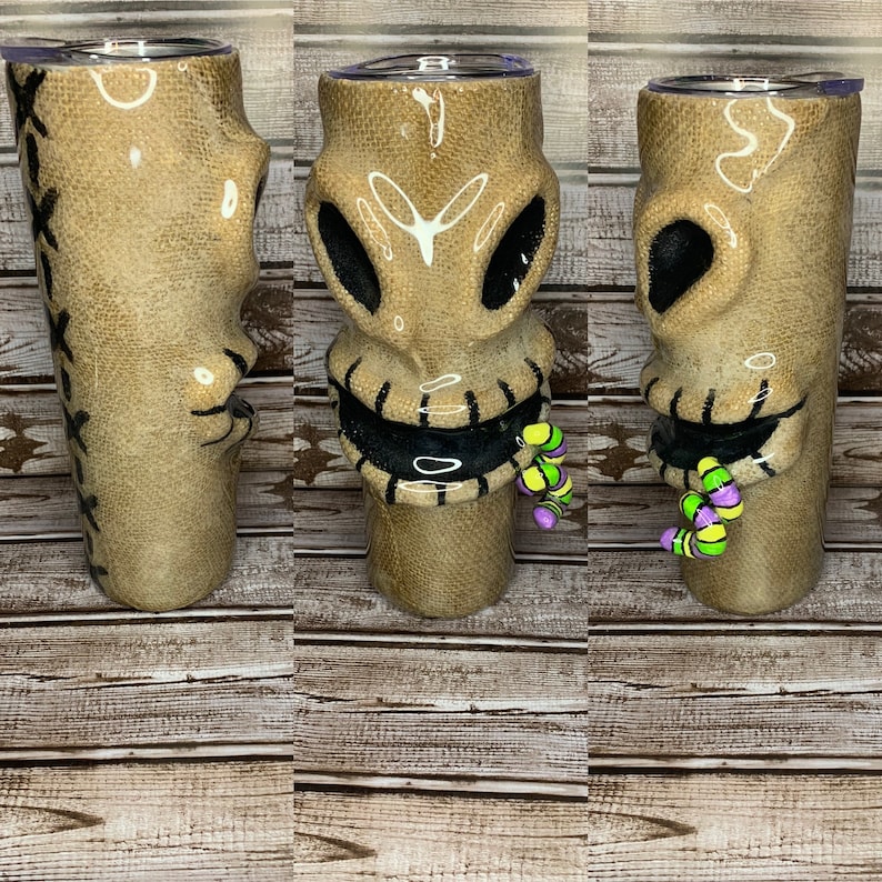 May include: A brown and black ceramic tumbler with a stitched mouth and eyes. The tumbler has a green and purple worm coming out of the mouth.