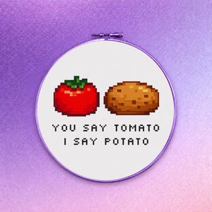Op de afbeelding: Een ronde borduurring met witte stof en een pixel art ontwerp van een rode tomaat en een bruine aardappel. Onder de groenten staat de zwarte, gepixelde tekst: YOU SAY TOMATO I SAY POTATO. Het frame van de borduurring is paars van kleur.