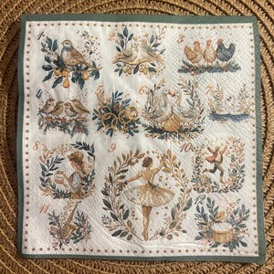 May include: A square, white paper napkin with a green border, featuring various illustrations of birds, geese, and a ballerina, surrounded by floral wreaths. The illustrations are in muted tones of brown, gold, and green.