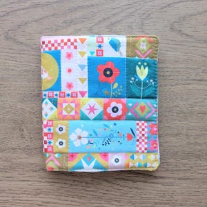 May include: A vibrant, quilted fabric coaster with a patchwork design. The coaster showcases floral and geometric patterns in blue, red, yellow, and pink. The edges are finished with a contrasting fabric.