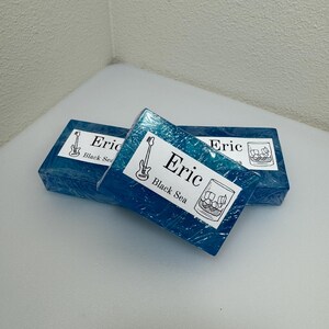 May include: Three blue soap bars with a white label. The label says "Eric Black Sea" and features a drawing of a guitar and a glass of ice.