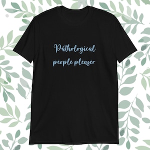 Könnte beinhalten: Schwarzes T-Shirt mit dem hellblauen Text "Pathological people pleaser" in einer kursiven Schriftart. Das Shirt ist ein kurzärmeliger Rundhals-Stil. Der Hintergrund zeigt grüne Blattmuster.