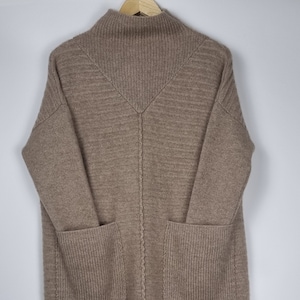 Może przedstawiać: Brązowy sweter z długimi rękawami, wysokim kołnierzem i dwiema kieszeniami. Sweter ma żebrowaną fakturę i lekko asymetryczny dół.