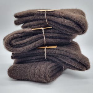 May include: A stack of four pairs of brown knitted socks, each pair tied with twine and a small brown tag. The socks have a ribbed texture and a soft, fuzzy appearance, suggesting a warm and comfortable material.