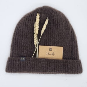 Könnte beinhalten: Eine braune Strickmütze mit gerippter Struktur. Die Mütze hat ein kleines braunes Etikett mit dem Text "PlanMix" darauf. Das Etikett hat auch ein kleines quadratisches Logo mit einem stilisierten "P" darin.