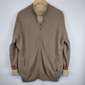 May include: A brown zip-up sweater with a beige lining and ribbed cuffs. The sweater has a high collar and two pockets.