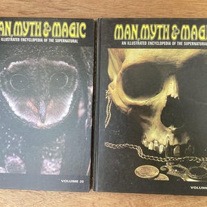 Puede incluir: Dos libros de tapa dura titulados "MAN MYTH & MAGIC: An Illustrated Encyclopedia of the Supernatural." El volumen 20 presenta un b&uacute;ho, mientras que el volumen 19 muestra una calavera con cadenas y monedas de oro. Los libros est&aacute;n sobre una superficie de madera.