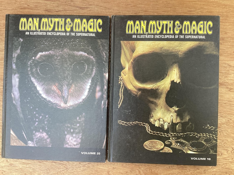 Puede incluir: Dos libros de tapa dura titulados "MAN MYTH & MAGIC: An Illustrated Encyclopedia of the Supernatural." El volumen 20 presenta un b&uacute;ho, mientras que el volumen 19 muestra una calavera con cadenas y monedas de oro. Los libros est&aacute;n sobre una superficie de madera.