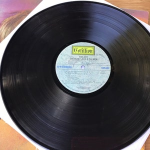 May include: Black vinyl record with a white label. The label has the text "Cotillion" and "Emerson, Lake & Palmer" with the album title "Trilogy" printed on it. The record is side one, stereo.