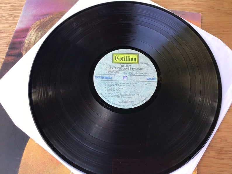 May include: Black vinyl record with a white label. The label has the text "Cotillion" and "Emerson, Lake & Palmer" with the album title "Trilogy" printed on it. The record is side one, stereo.