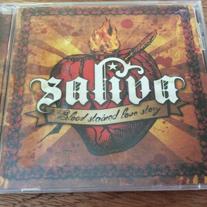 Może przedstawiać: Pudełko na płytę CD z czerwono-ż&oacute;łto-czarnym wzorem. Pudełko przedstawia stylizowane serce z płomieniami i tekstem "Saliva Blood Stained Love Story".
