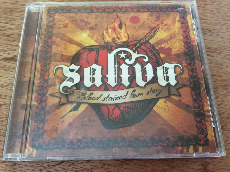 Może przedstawiać: Pudełko na płytę CD z czerwono-ż&oacute;łto-czarnym wzorem. Pudełko przedstawia stylizowane serce z płomieniami i tekstem "Saliva Blood Stained Love Story".