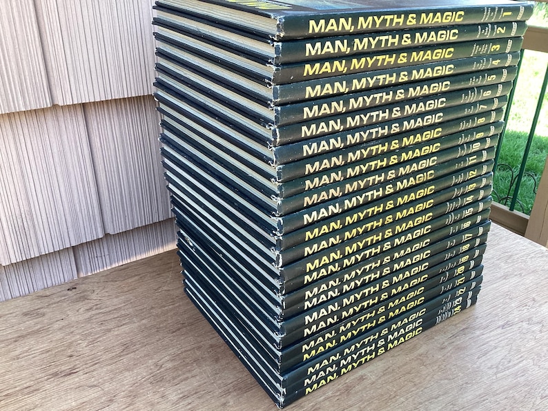 Puede incluir: Una pila de libros de tapa dura con el t&iacute;tulo "MAN, MYTH & MAGIC" en letras doradas sobre una cubierta verde oscuro. Los libros est&aacute;n apilados sobre una superficie de madera junto a una pared clara y texturizada.