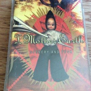 May include: A cassette tape with a red, gold and white design. The image features a doll with a striped shirt and black trousers. The text on the tape reads "I Mother Earth" and "Scenery and Fish".