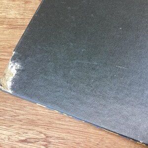 Puede incluir: Un objeto rectangular azul oscuro con una superficie texturizada. La esquina muestra desgaste con material claro expuesto. El objeto descansa sobre una superficie de madera.