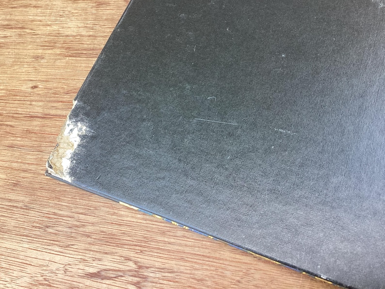 Puede incluir: Un objeto rectangular azul oscuro con una superficie texturizada. La esquina muestra desgaste con material claro expuesto. El objeto descansa sobre una superficie de madera.