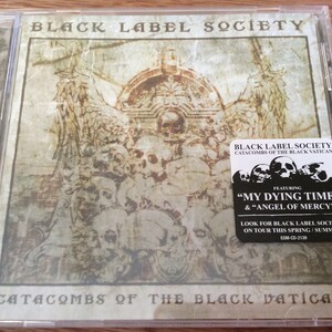 Może przedstawiać: Pudełko na płytę CD z czarno-białym obrazkiem czaszki i skrzyżowanych kości. Tekst na pudełku brzmi "Black Label Society Catacombs of the Black Vatican".