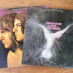 May include: Two vinyl records by Emerson, Lake & Palmer. The first record features a photo of two men with long hair. The second record features a white dove flying against a dark background.
