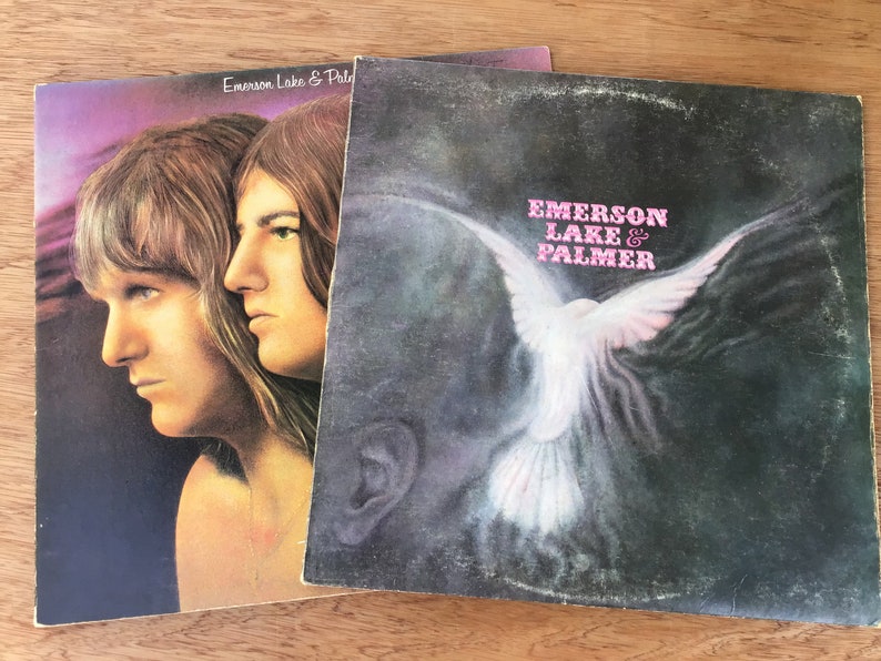 May include: Two vinyl records by Emerson, Lake & Palmer. The first record features a photo of two men with long hair. The second record features a white dove flying against a dark background.