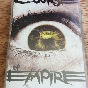 May include: A cassette tape featuring a close-up image of a large eye with a yellow iris. The text "Course of Empire" is printed in black on the front of the cassette tape.