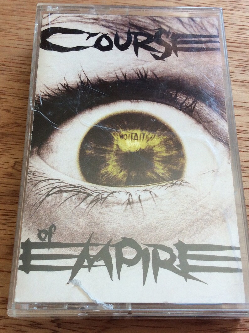 May include: A cassette tape featuring a close-up image of a large eye with a yellow iris. The text "Course of Empire" is printed in black on the front of the cassette tape.