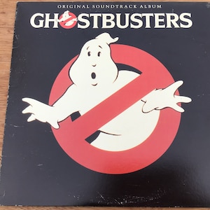 May include: A black vinyl record album cover with the title "Ghostbusters" in white letters. The cover features a red circle with a diagonal line through it, and a white ghost with a surprised expression.