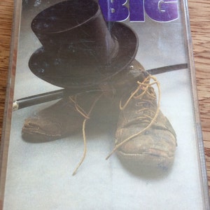 May include: A cassette tape featuring a black top hat and two brown leather shoes. The cassette tape cover has the text "MR. BIG" in purple letters.