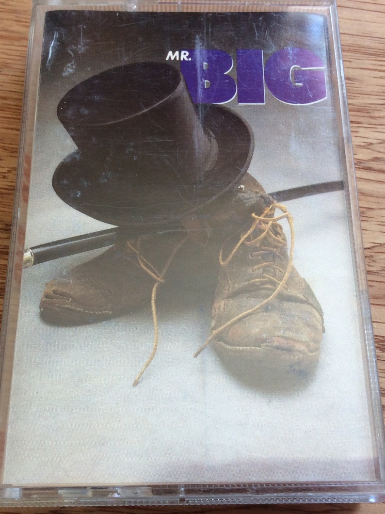 May include: A cassette tape featuring a black top hat and two brown leather shoes. The cassette tape cover has the text "MR. BIG" in purple letters.
