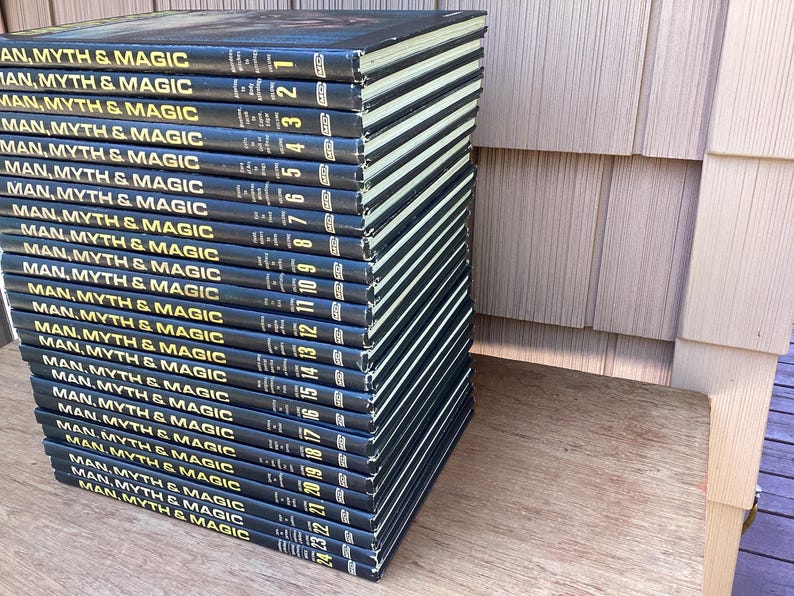 Puede incluir: Una pila de veintitr&eacute;s libros de tapa dura titulados "Man, Myth & Magic". Los libros tienen cubiertas azul oscuro con letras y n&uacute;meros dorados. Los lomos son visibles, mostrando el t&iacute;tulo de la serie y los n&uacute;meros de volumen.