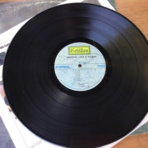 May include: Black vinyl record with a blue and white label. The label says "Cotillion" and "Emerson, Lake & Palmer". The record is labelled "Two" and lists the songs "The Three Fates", "Knife Edge", "Lucky Man", "Still... You Turn Me On", "From The Beginning", "Jeremy Bender", "Take A Pebble", "The Endless Enigma", "Close To Home", "The Battle Of Epping Forest", "Hoedown", "Lucky Man (Reprise)", "The Endless Enigma (Reprise)", "From The Beginning (Reprise)".