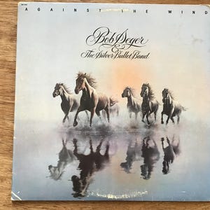 May include: Album cover for Bob Seger & The Silver Bullet Band's "Against the Wind." The cover art features a painting of six brown horses running through water, with their reflections visible. The album title and artist name are in elegant script.