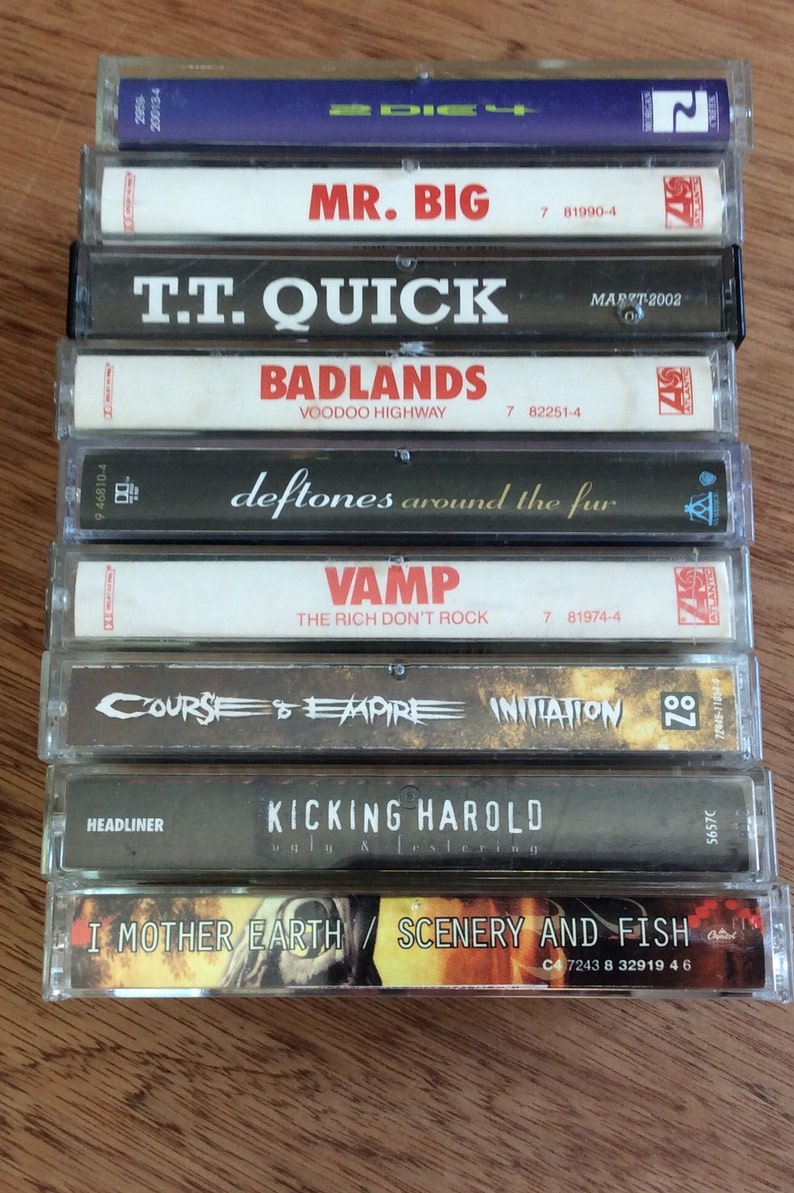 May include: A stack of nine cassette tapes featuring a variety of artists and album titles. The tapes are housed in clear plastic cases with black and white labels. The artists include Mr. Big, T.T. Quick, Badlands, Deftones, Vamp, Course of Empire, Kicking Harold, and I Mother Earth.