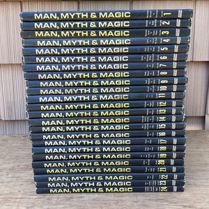 Puede incluir: Una pila de 24 libros titulados "MAN, MYTH & MAGIC" con letras doradas sobre una cubierta negra. Cada libro est&aacute; numerado en el lomo. Los libros est&aacute;n apilados sobre una superficie de madera.